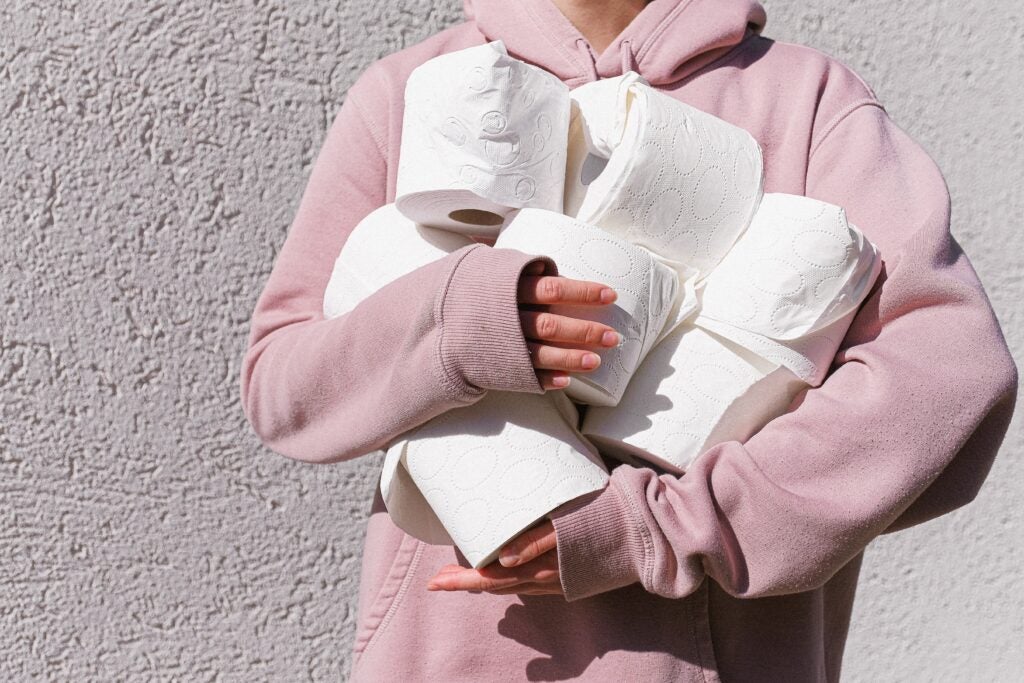 Person in pink sweatshirt holding toilet paper rolls