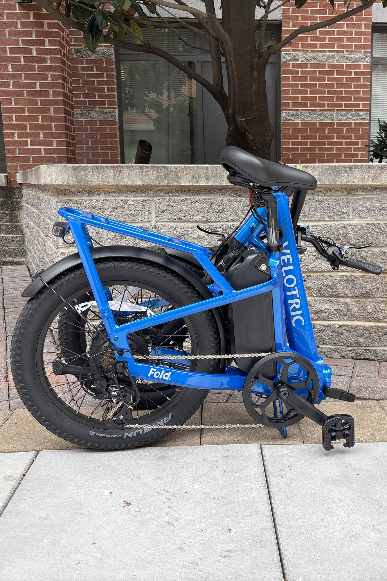 Gros plan latéral d'un pli vélotrique bleu 1 plus d'évike pliant complètement plié devant un mur de pierre gris