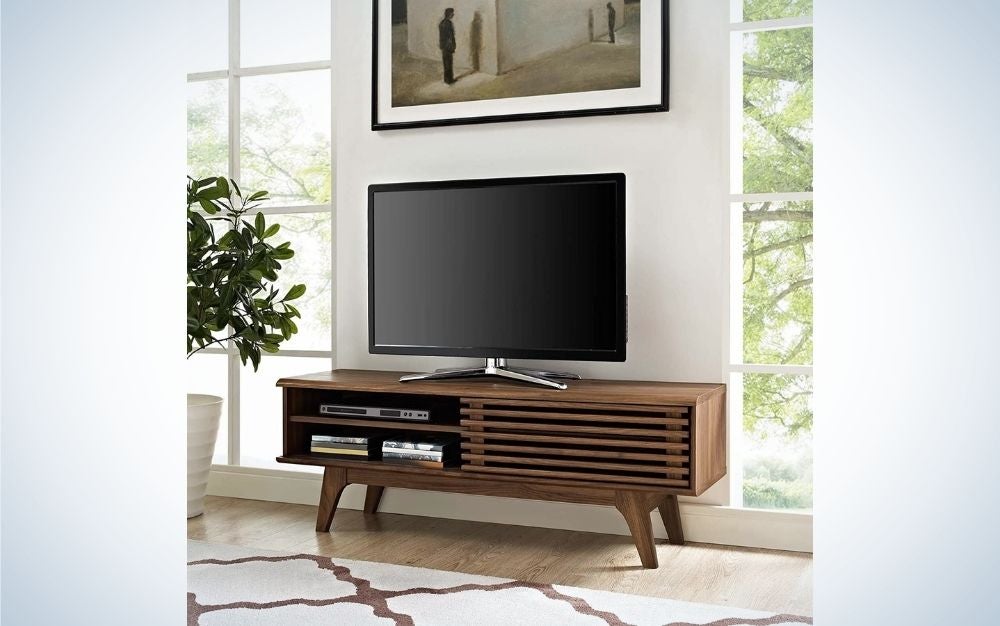 Un cuadro cuelga de la pared blanca y un televisor LED grande se encuentra en un soporte de madera laminado para TV.