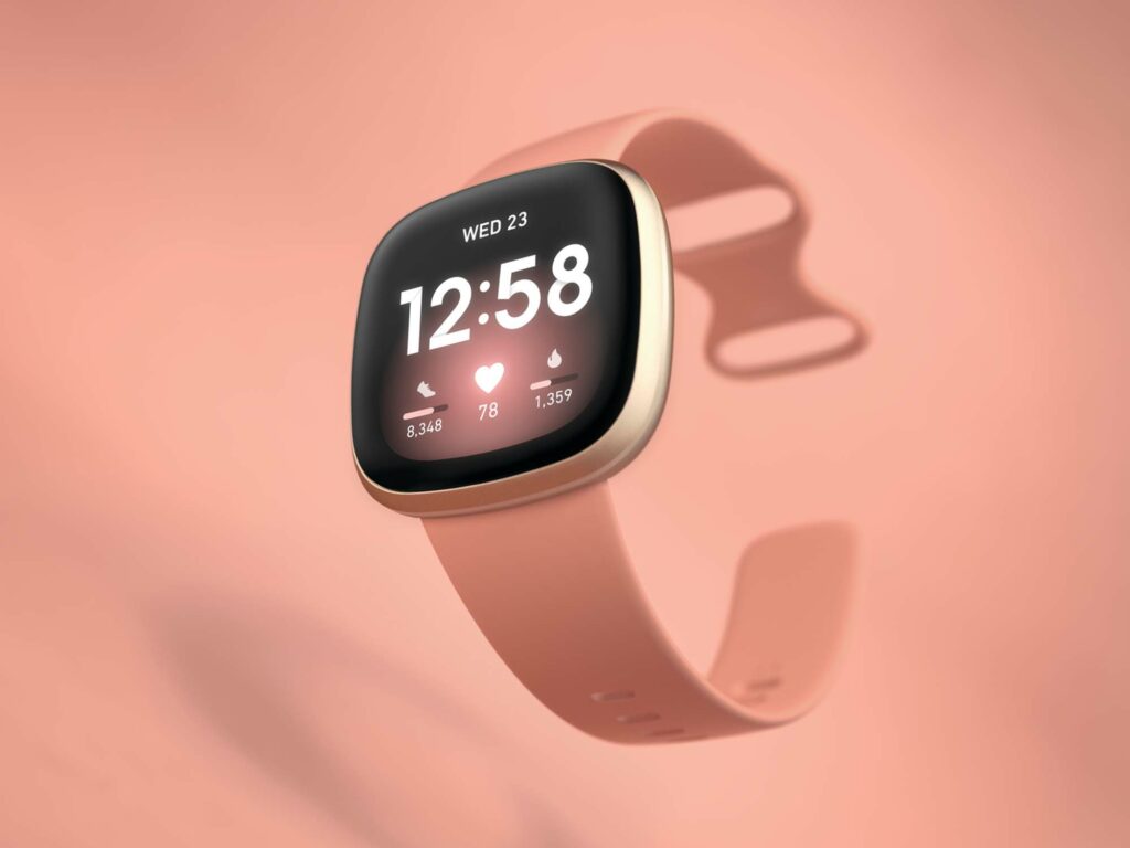 A Fitbit Versa 3 on a pale pink background.