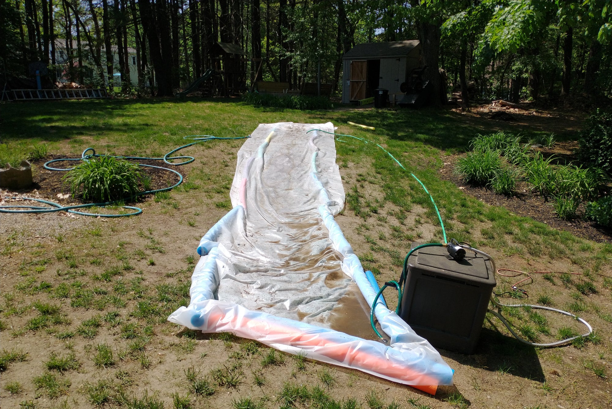 A DIY slip and slide in a yard, with a pump and hose to recycle the water.
