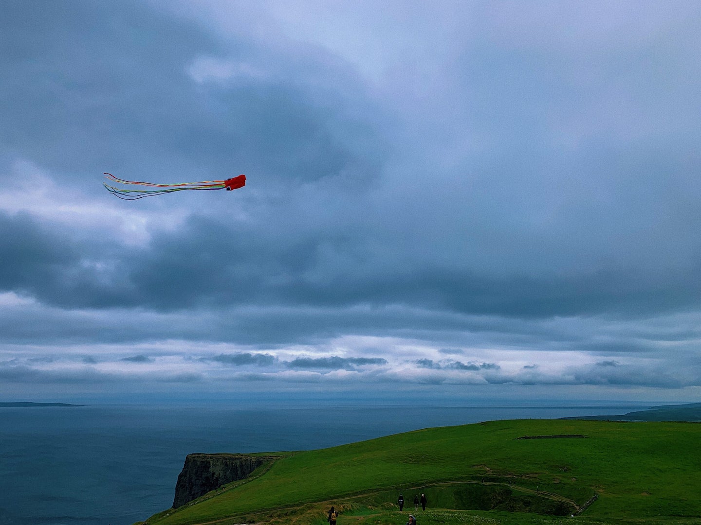 A kite flying above a seaside cliff under cloudy skies.