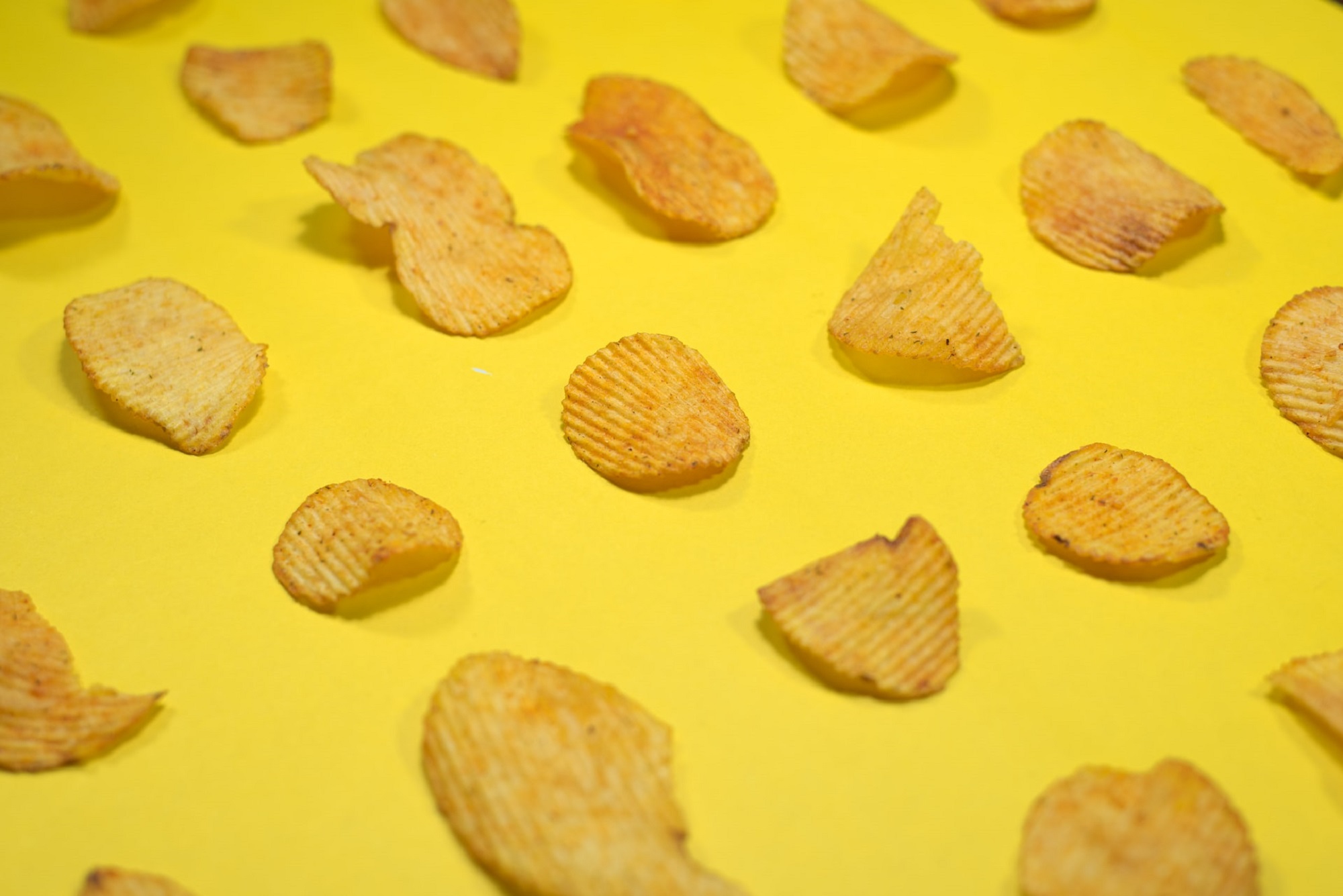 Salty ridged potato chips on yellow background