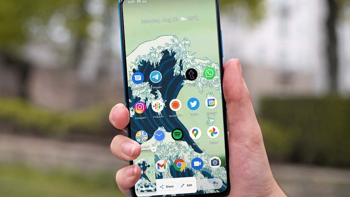 A hand holding an Android phone and taking a screenshot while outdoors in a park.