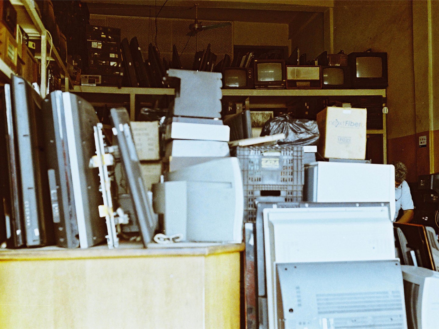 A dim room with a lot of old computers, TVs, and other technology piled up on shelves.