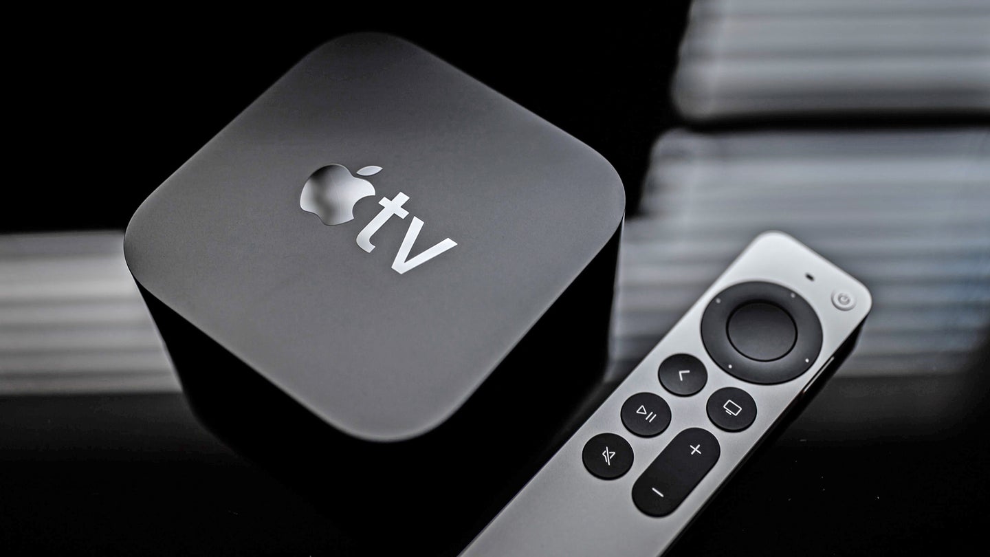A black Apple TV 4K box on a black surface next to an Apple TV remote.