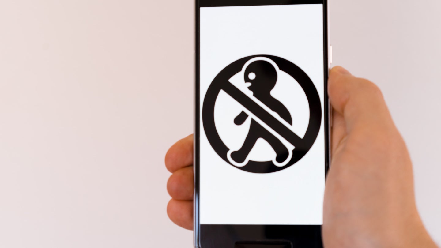 A person holding a smartphone with a crossed-out image of a person's silhouette on it.