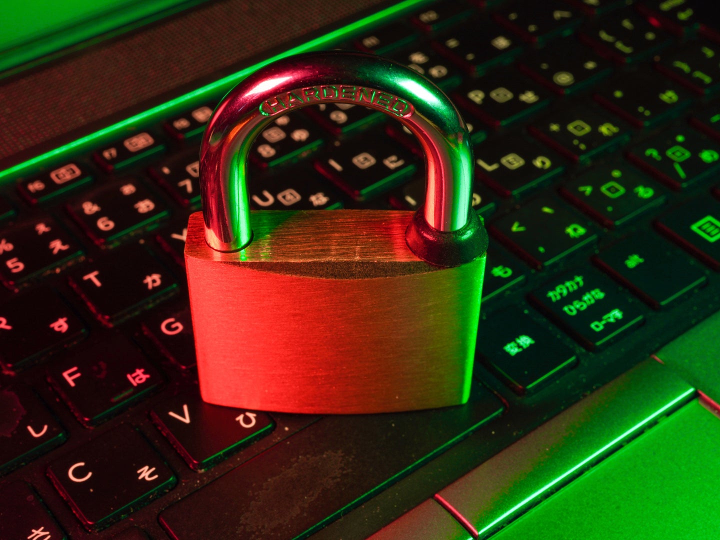 A large padlock sitting on a computer keyboard under some green and red lighting.