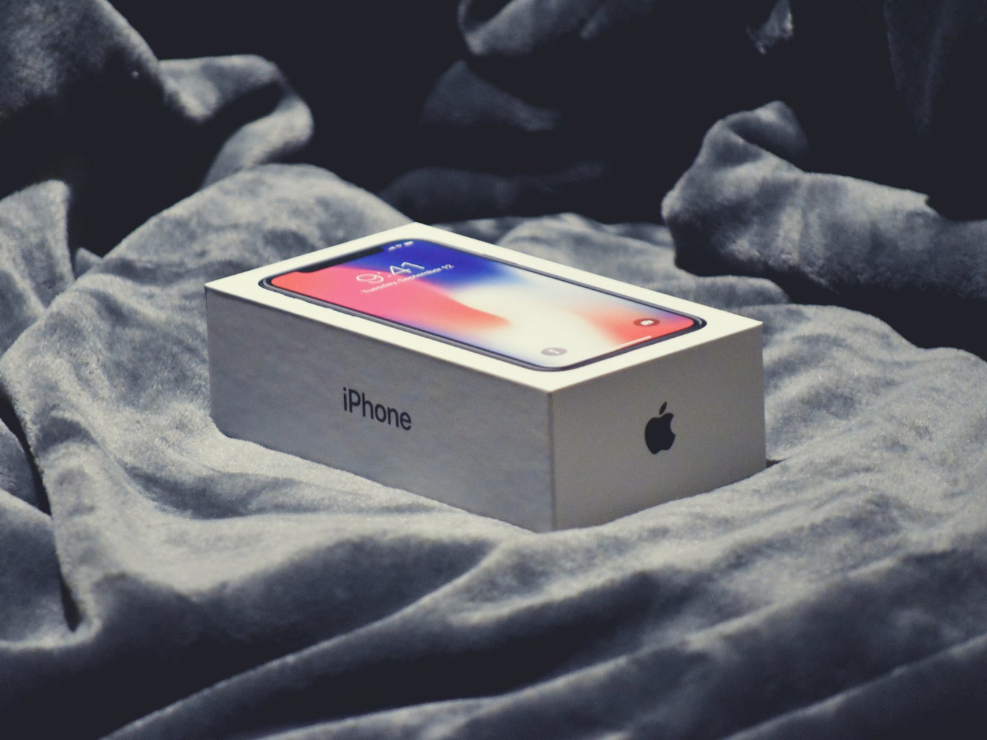 An Apple iPhone in a box, on a lush bed of soft gray blankets.