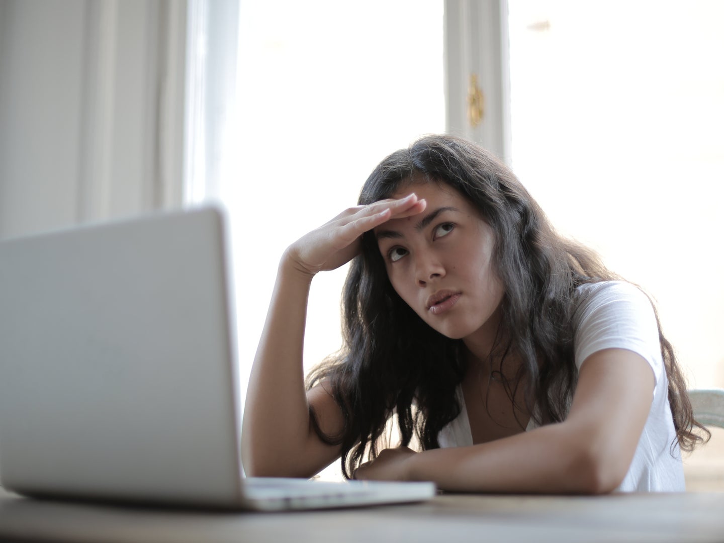 A woman leaning over a laptop computer, annoyed, with her hand on her forehead.