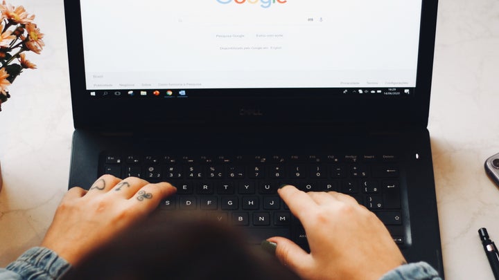 A person typing on a laptop with the Google search engine on the screen.