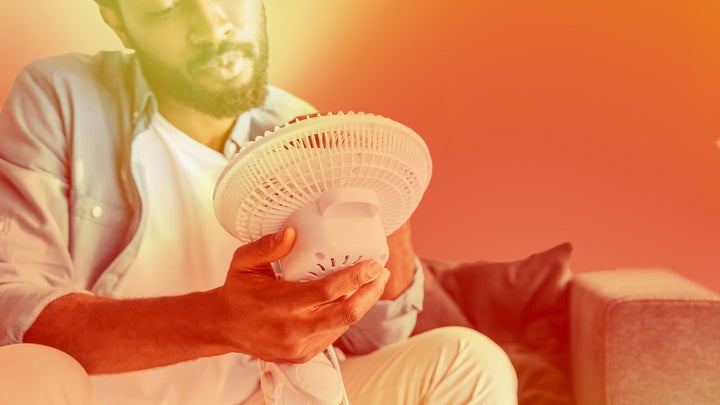 A man sitting and holding an electric fan in front of his face.