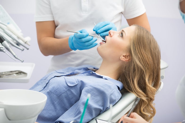a dentist examines to mouth of a reclining teenage girl
