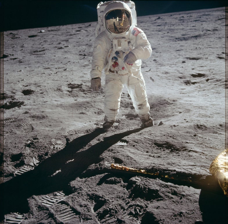 an astronaut stands on the gray surface of the moon in a spacesuit