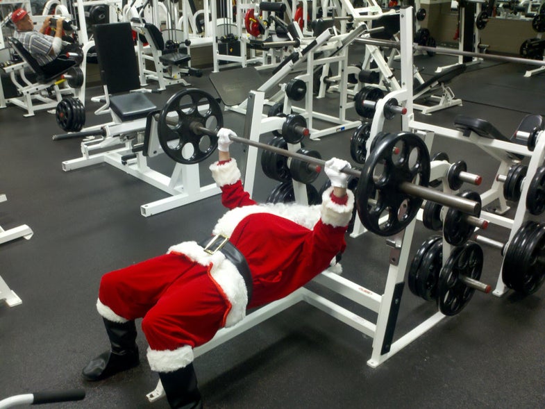 Person at gym dressed in a Santa suit doing a holiday workout on the bench press