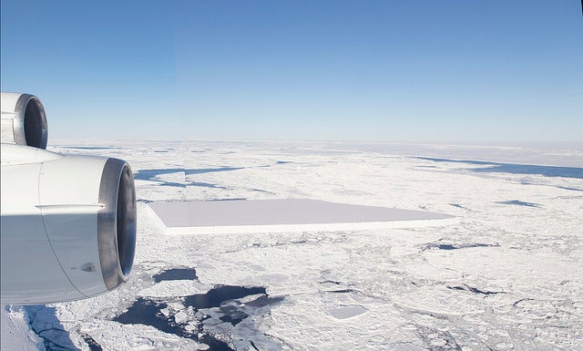Aerial shot of a flat, rectangular iceberg floating in a sea of smaller pieces of ice.