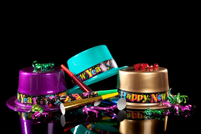 three colorful plastic hats that say happy new year on a black background with noisemakers and ribbons