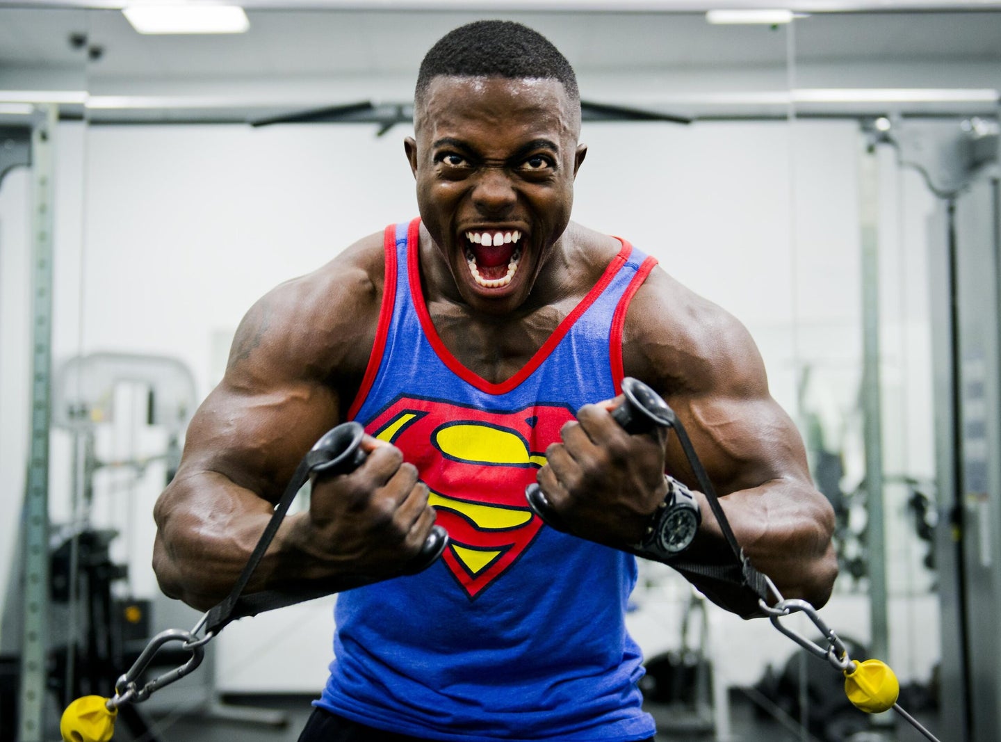 Black body builder in a Superman tank yelling as they pull arm weights to keep their New Year's resolution to stay fit