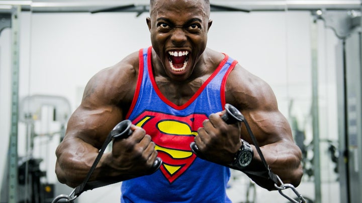Black body builder in a Superman tank yelling as they pull arm weights to keep their New Year's resolution to stay fit