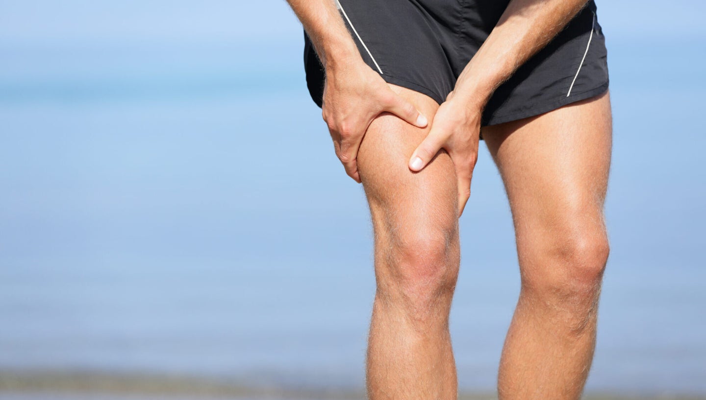 A person wearing running shorts holding their thigh on a beach, potentially wondering what happens when you pull a muscle, because they probably just did.