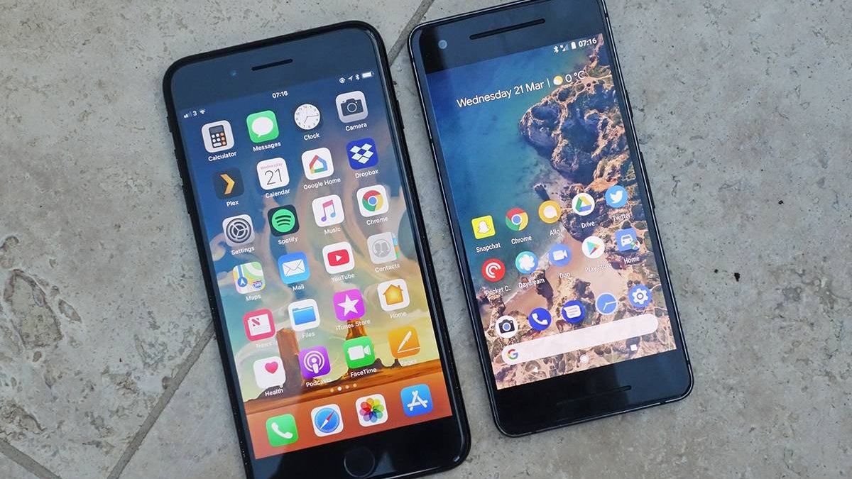 An Android phone and an iPhone next to each other on a gray tile floor.