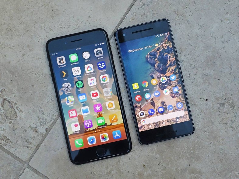 An Android phone and an iPhone next to each other on a gray tile floor.