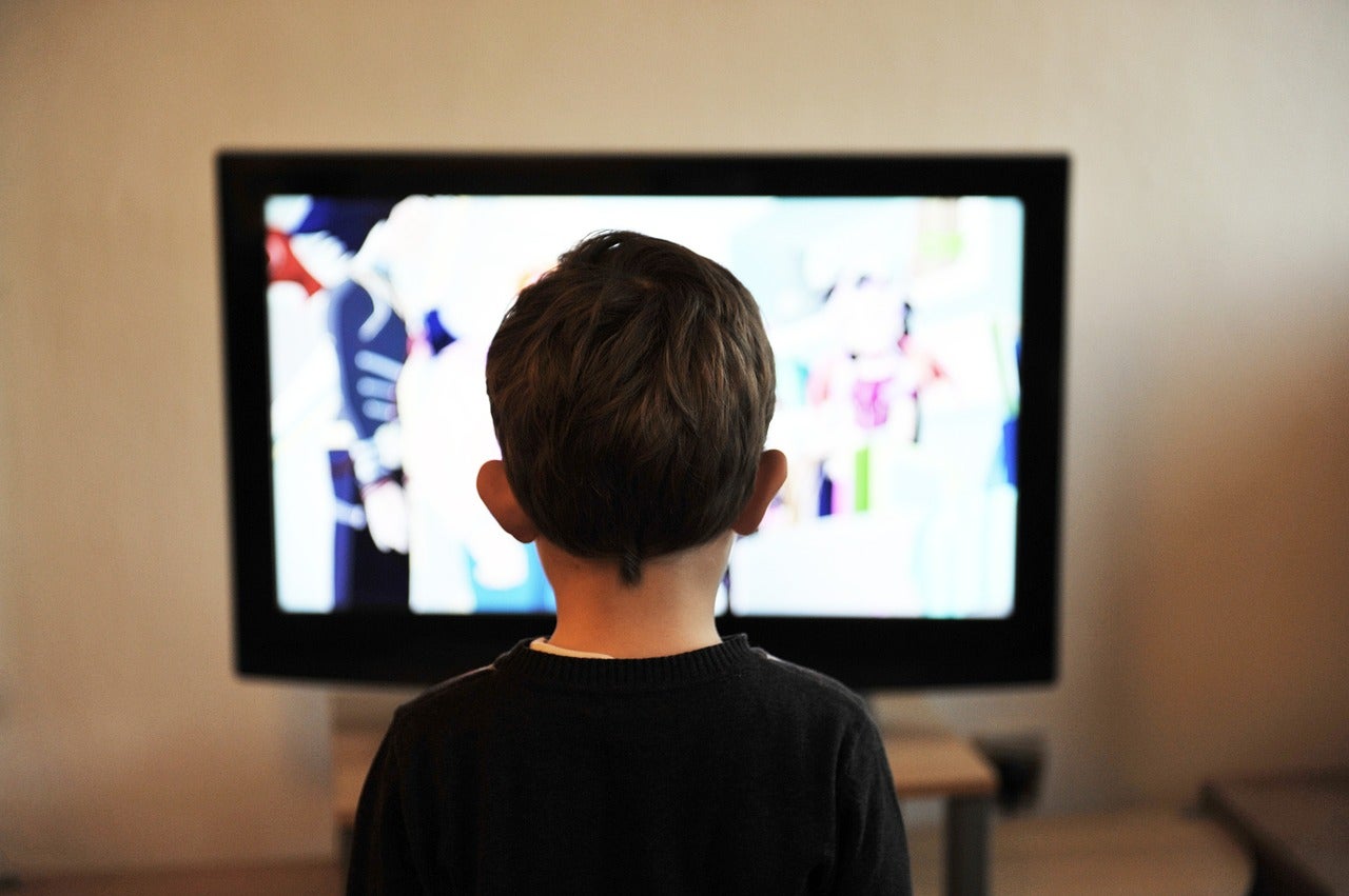 A child standing in front of a TV, watching a show or a movie.