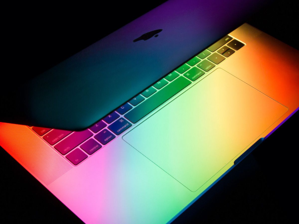 A partially open MacBook in the dark, with multi-colored lights shining from the screen.