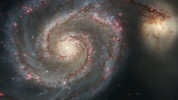 a large spiral galaxy next to a smaller ball of light in space