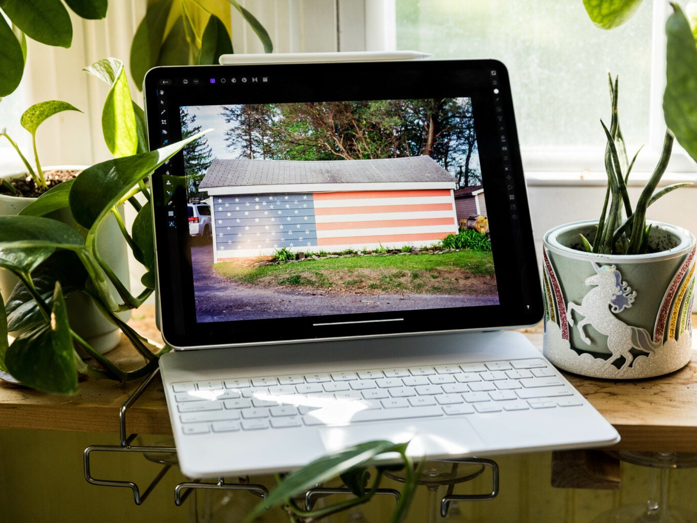 An iPad Pro with a keyboard, on a windowsill surrounded by plants and bathed in sunlight.