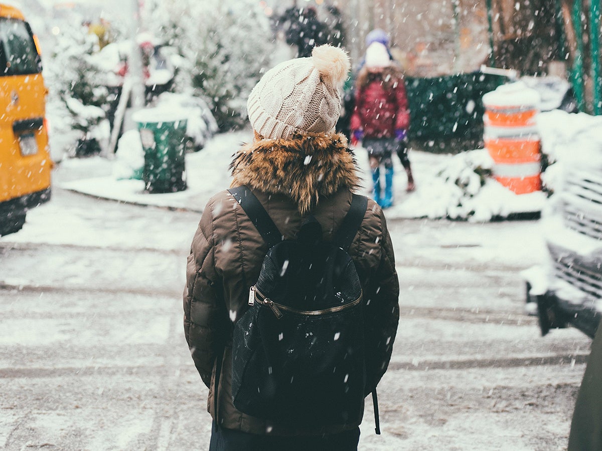 Een persoon die aan de kant van een straat staat terwijl er in de winter sneeuw valt.