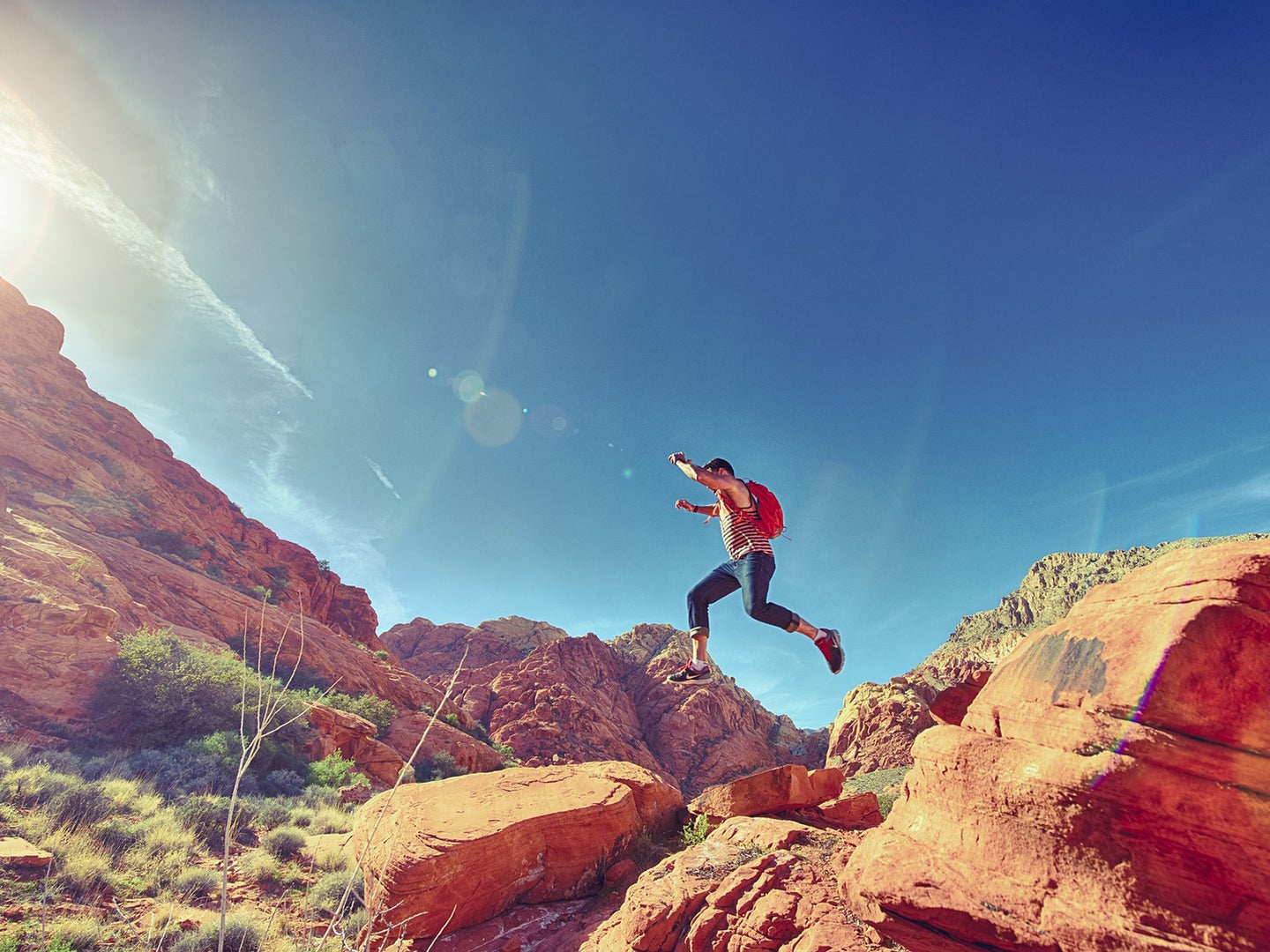man jumping down red rocks