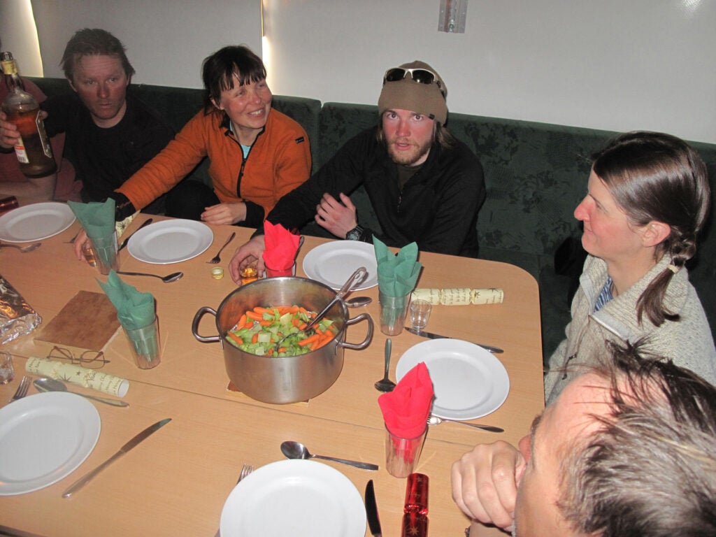 Inside the "living module," team members celebrate Christmas on the Polar Plateau with a dinner party. From left: Svein Heinrickson (mechanic), Anna Sinisalo (shallow radar specialist), Andreas Tollefson (engineer), Kirsty Langley (deep radar specialist), and Stein Tronstad (GIS and mountaineering expert). Heinrickson is holding a bottle of <em>linie</em> aquavit, the legendary Scandinavian liquor (the name <em>linie</em> means that the cask has crossed the Equator).