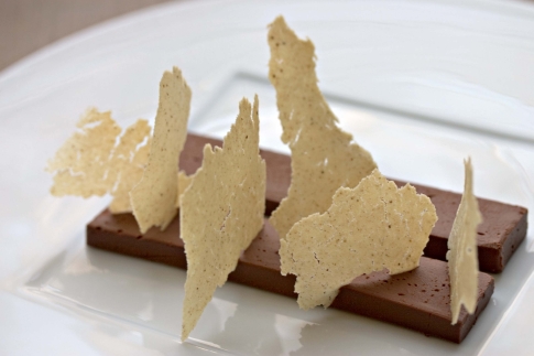 Some chocolate bars with jagged banana crisps stuck vertically into them, on a white plate.