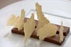 Some chocolate bars with jagged banana crisps stuck vertically into them, on a white plate.