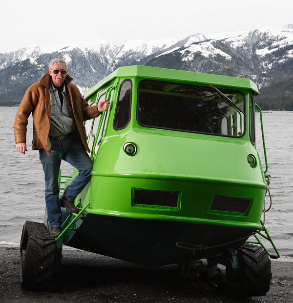 Stan Hewitt standing on the wheels of his homemade amphibious vehicle.
