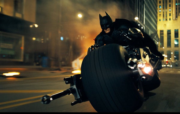 Even outside the world of the film fantasy, this is one pretty fantastic vehicle, but what about the fictional Batmobile? It has a some features not currently found on the prototypes – missile launchers, machine guns, bullet proof armor plating, and several fully automated modes such as "loiter", "intimidate", and "stealth". In addition in <em>The Dark Knight</em>, we are introduced to the "Batpod"—that motorcycle-like vehicle that can be ejected from the left side of the vehicle. After the car undergoes a "catastrophic failure" following a run-in with a 20-ton tractor trailer, the Batpod gets spit out for the first time into the streets of Gotham. (We'll discuss that collision below.) Now in <em>Batman Begins</em> there was a brief scene where the Batmobile apparently engages a cloaking device while in "stealth" mode. The vehicle completely disappears from the view of pursuing vehicles for a few seconds after Batman pushes a button on the dashboard. It was a little disappointing that this feature didn't appear in the sequel because as implausible as it may seem, <a href="https://www.popsci.com/scitech/article/2008-08/invisibility-cloak-swirls-closer-reality/">recent research</a> into a fascinating new class of materials called "metamaterials" suggests that this may actually eventually be feasible. These fabricated materials strangely have negative refractive indices for specific frequencies of electromagnetic radiation. When light or other frequencies of e-m radiation enter a "normal" material at an angle to the surface, the waves refract outwards at a higher angle. For a metamaterial, with its bizarre negative index of refraction, the waves are bent inward. Let's say you have a pear sitting on a table behind a piece of metamaterial. The general idea is that unlike with normal materials (where the light coming from the pear will either be reflected off of the material or refracted outward), in metamaterials the light rays diverging from the pear with actually bend around the metamaterial and re-converge. The result is the light from the pear will_ appear_ to be travelling directly towards you. You'll see the pear but not the obstruction in front of it! Laboratory experiments using single frequencies of microwave radiation have demonstrated this phenomenon successfully, however they don't yet know how to make a metamaterial that will work simultaneously with multiple frequencies, or for frequencies in the visible spectrum. Even if it could be figured out, though, there is still would be a drawback: While someone outside a metamaterial Batmobile can't see in, someone inside also can't see out. This could make driving in traffic a problematical proposition even for Batman.