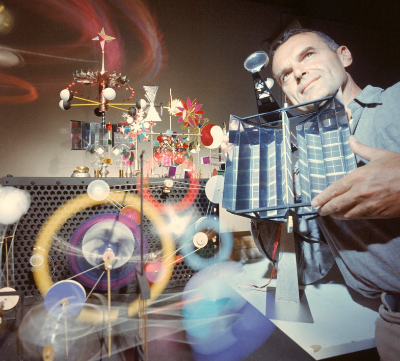 Architect & designer Charles Eames holding "engine" which generates solar power to run the toys surrounding him.