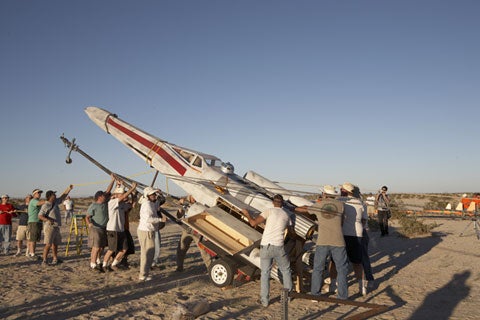 A homemade Star Wars X-wing fighter rocket surrounded by people in a desert.