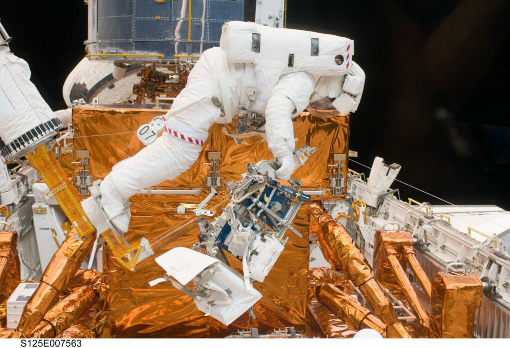 Astronaut Michael Good works with the Hubble Space Telescope in the cargo bay of the Space Shuttle Atlantis