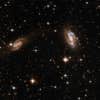 This system consists of two interacting spiral galaxies. The galaxy to the left displays a dim plume of luminosity that extends to the right in the direction of the second spiral. Both galaxies are partly obscured by dust lanes. The galaxy at center is adorned with blue knots of stars. IRAS 18090+0130 is located in the constellation of Ophiuchus, the Serpent Holder, some 400 million light-years away from Earth.