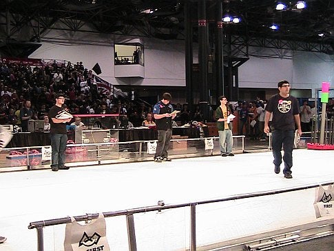A few people in an arena in front of a crowd at the 2009 FIRST Robotics Competition in New York City.