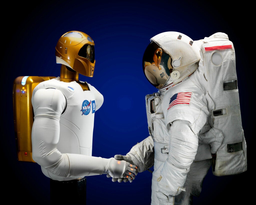 Robonaut 2 shakes the hand of a fellow astronaut.