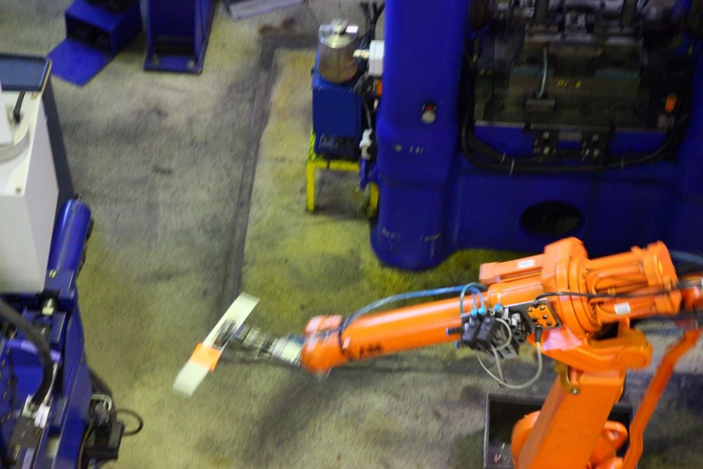 A robot arm rapidly grabs an upset-forged blank from the machine...