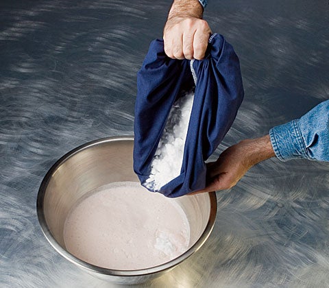 A person pouring a pillowcase full of dry ice into a bowl of ice cream ingredients.