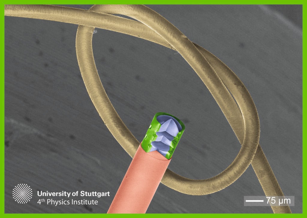 The 3D printed microlens mounted on a fiber optic cable and compared to a human hair.