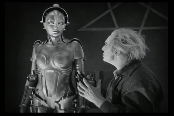 This still from Fritz Lang's classic urban nightmare <em>Metropolis</em> depicts the robotic alter ego of the angelic Maria, a pseudo-Christian reformer whose efforts to evangelize the city's cog-like workers infuriates their autocratic ruler, Joh. The new Maria, built by Rotwang (at right) on Joh's orders, is an exotic dancing sex fiend who, despite her debasement, manages to foment revolution even more effectively than before. Who'd have thought that the proletariat would prefer sex to god if allowed to choose their opiate?