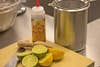 Halved lemons and limes on a wooden cutting board near a bottle of agave nectar and a knife.