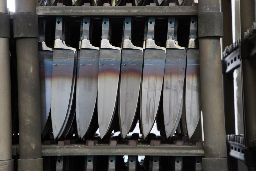 A rack of knives that have been forged and cut, but still not ground.