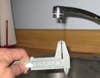 A sink faucet with a thin stream of water coming out of it and a person measuring the water's width with calipers.